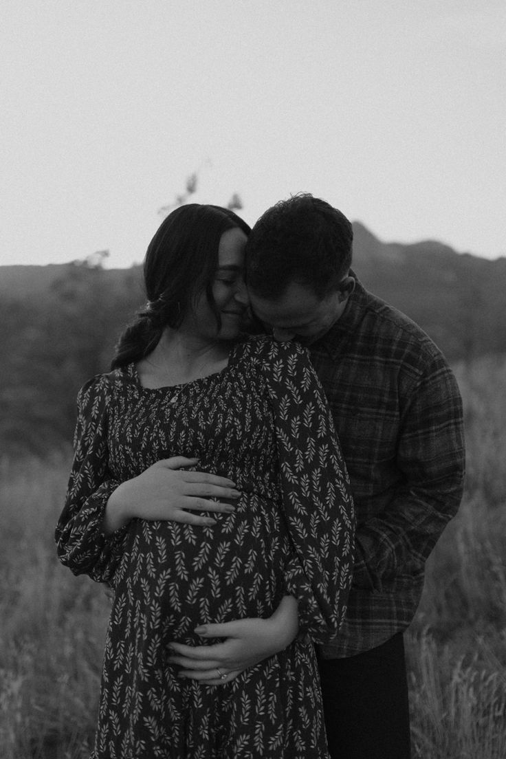 a pregnant couple cuddles while standing in a field