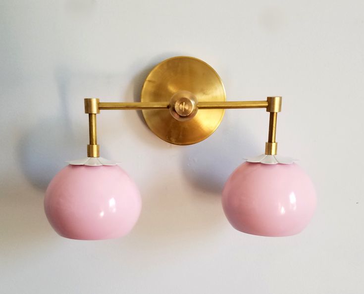 two pink and gold wall lights mounted on a white wall next to a light fixture