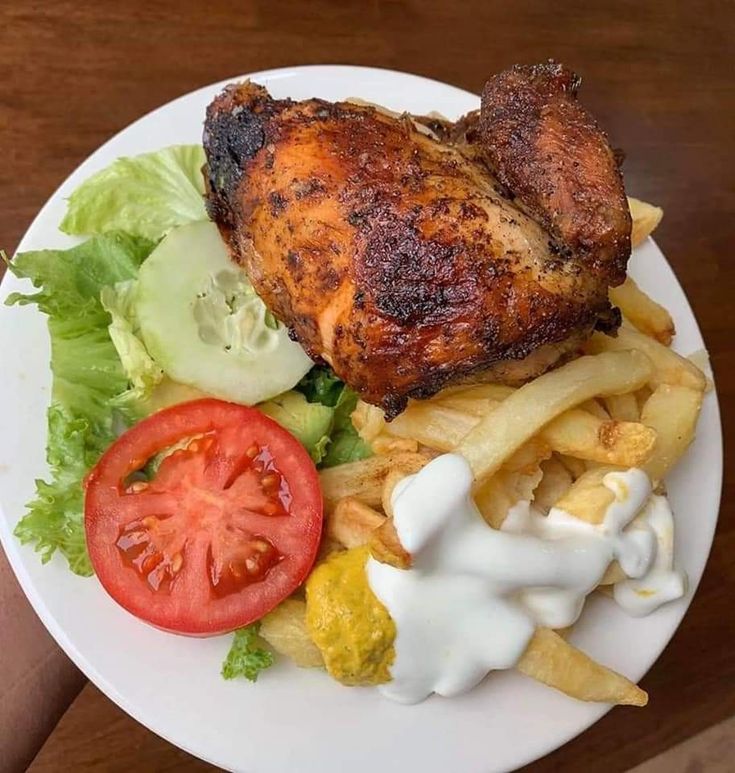 a white plate topped with chicken, french fries and tomatoes next to lettuce