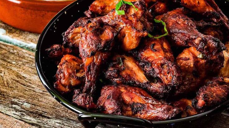 a bowl full of chicken wings next to a plate of rice on a wooden table