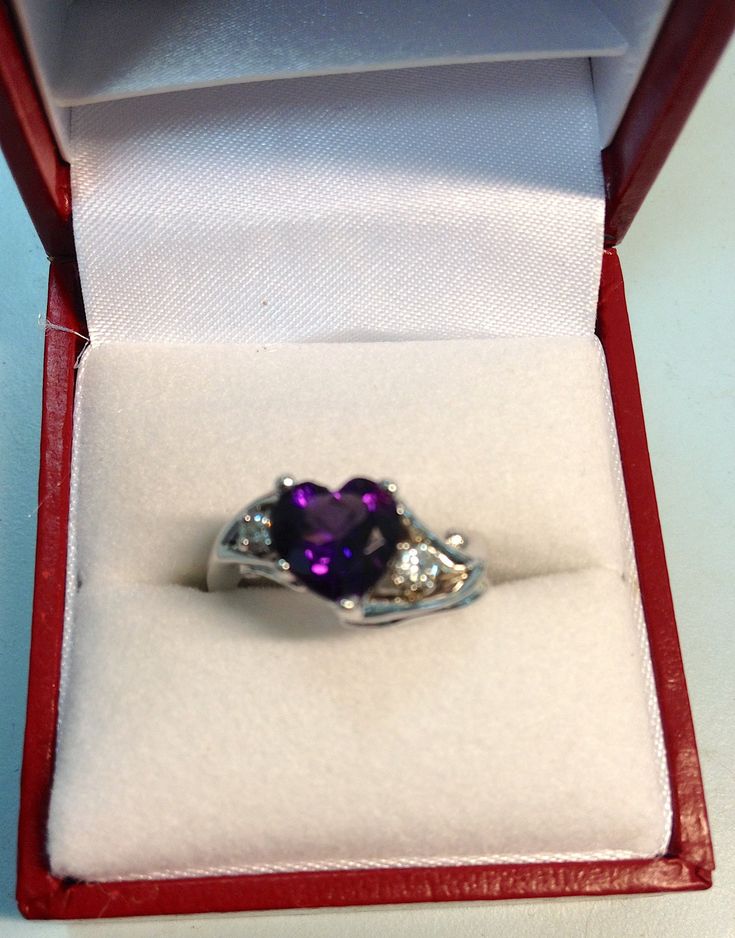 This beautifully handcrafted ring is one-of-a-kind and a gorgeous custom piece of jewelry to add as an everyday item or for an engagement/wedding occasion. It was designed by an artist, then produced by a talented local jeweler in Miami. The main stone is a heart-shaped Amethyst, with white diamonds on either side. In addition, the white gold band features hearts on the front and back. Anyone who wears it will be proud to do so!  Detailed specifications: *Amethyst heart-cut center stone *Round cut diamonds (.14 ct total for 2) *14K white gold band (resizing is possible) Purple Heart Ring, Amethyst Gem, Purple Band, Handcrafted Rings, Purple Heart, White Gold Band, Everyday Items, Gold Band, White Diamonds