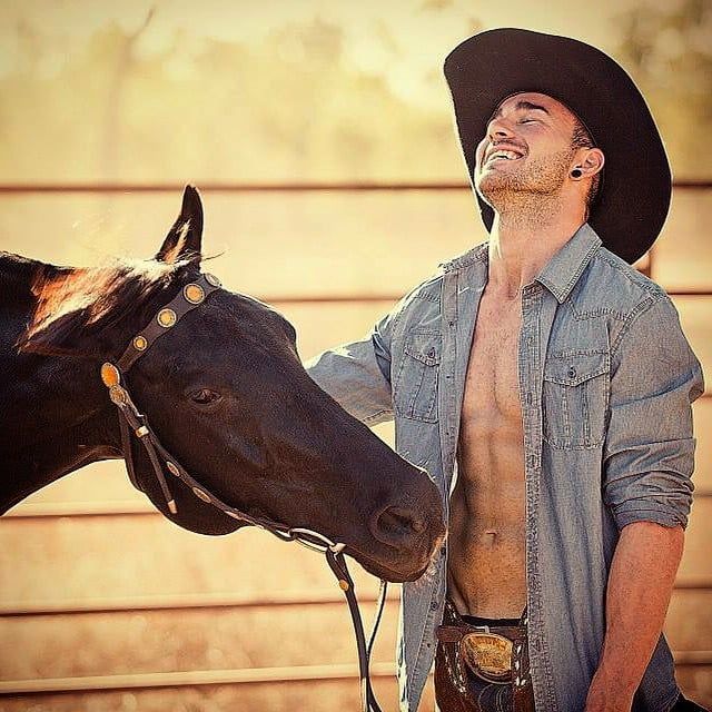 a man wearing a cowboy hat standing next to a horse with his mouth open and tongue out