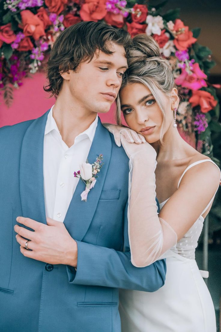 a man in a blue suit standing next to a woman wearing a white dress and holding her arm around her shoulder