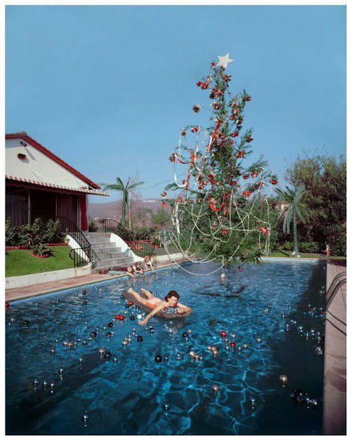 a woman swimming in a pool next to a christmas tree with red balls on it