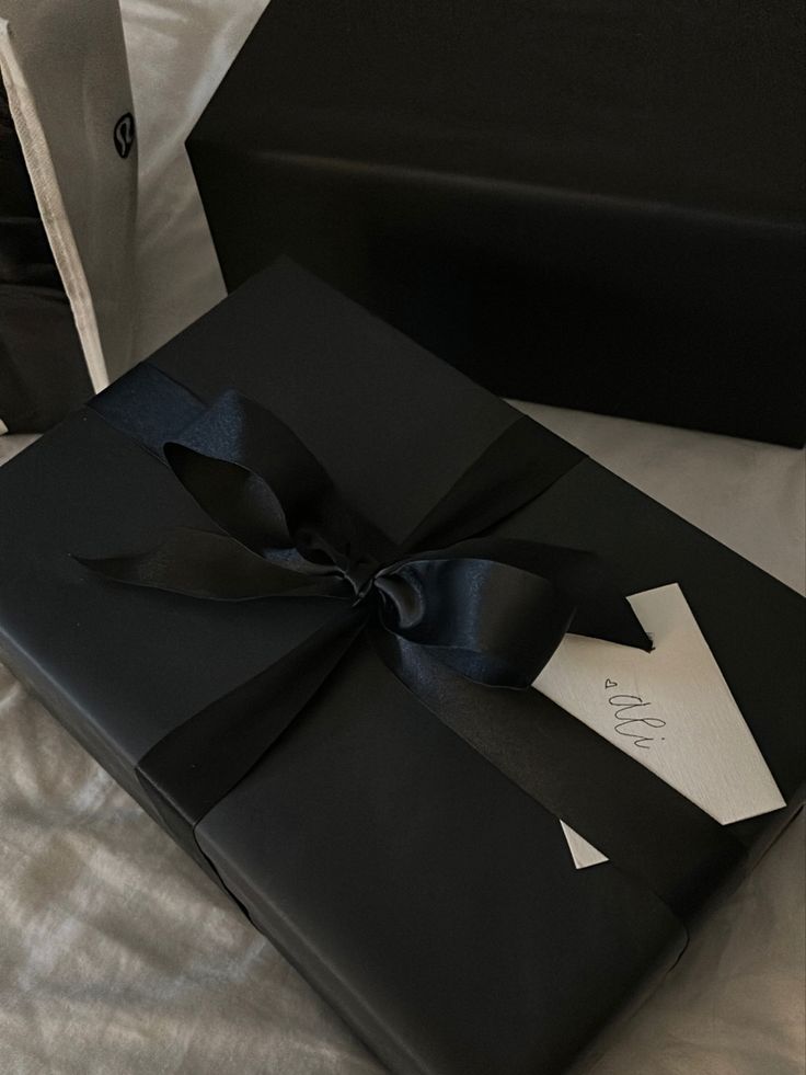 a black gift box with a bow on it sitting on top of a white sheet