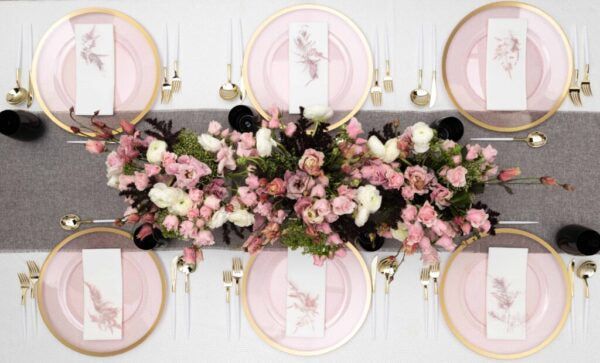 the table is set with pink and white plates, silverware, and floral centerpieces