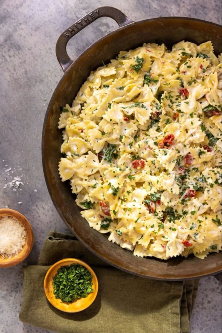 a pan filled with pasta and vegetables next to two small bowls