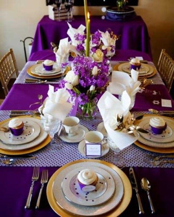 the table is set with purple and white plates, silverware, and flowers in vases