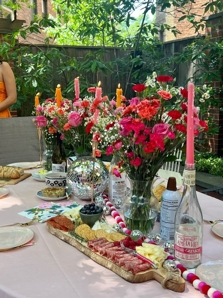 a table topped with lots of food and flowers next to bottles of wine on top of a white table cloth