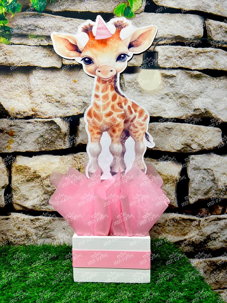 a baby giraffe standing on top of a pink present box in front of a stone wall