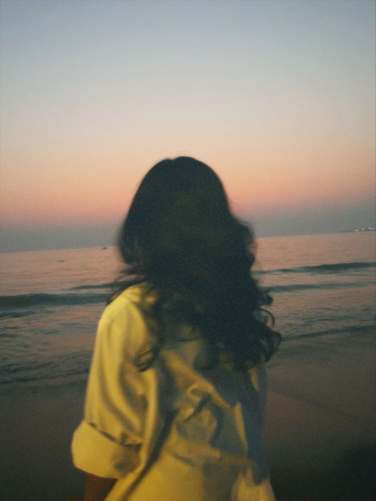 a woman standing on top of a sandy beach next to the ocean at sunset or dawn