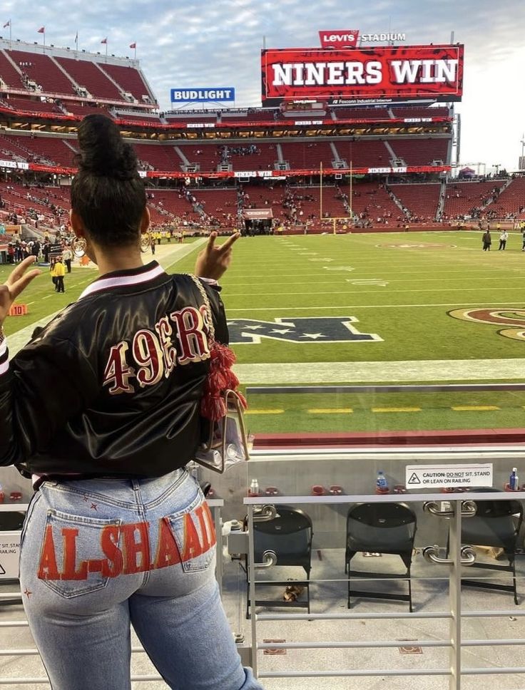 a woman standing on top of a field in front of a football stadium filled with people