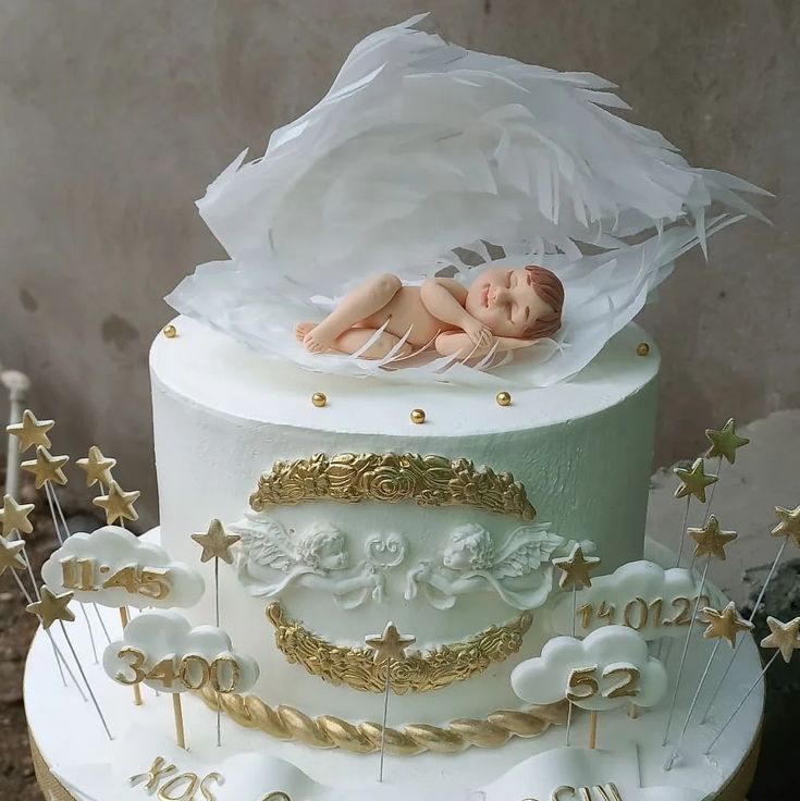 there is a white cake with gold decorations and a sleeping baby on the top tier