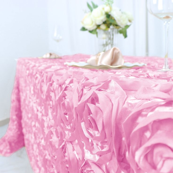 a pink table cloth with flowers on it and wine glasses next to it, in front of a white wall