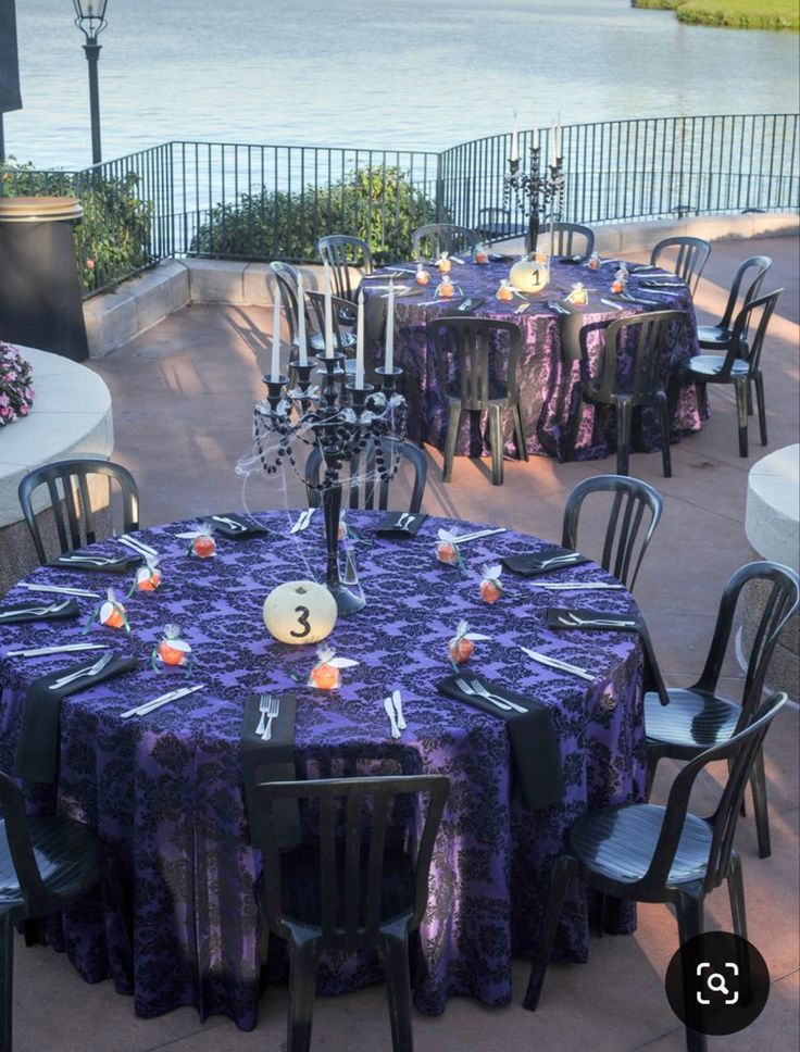 an outdoor dining area with purple tablecloths and black chairs, overlooking the water