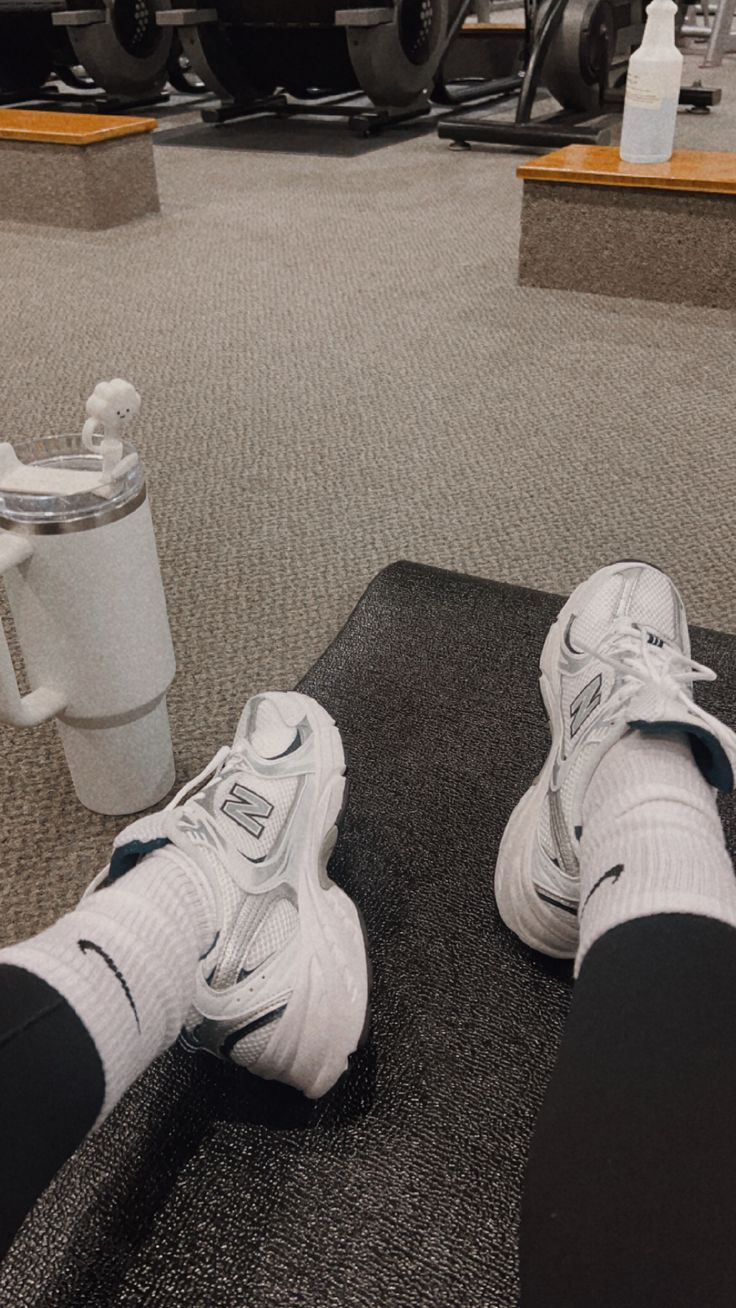 a pair of white sneakers sitting on top of a black mat next to a coffee cup