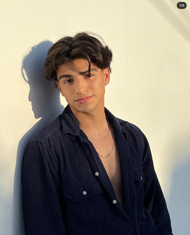 a young man standing in front of a white wall with his shadow on the wall