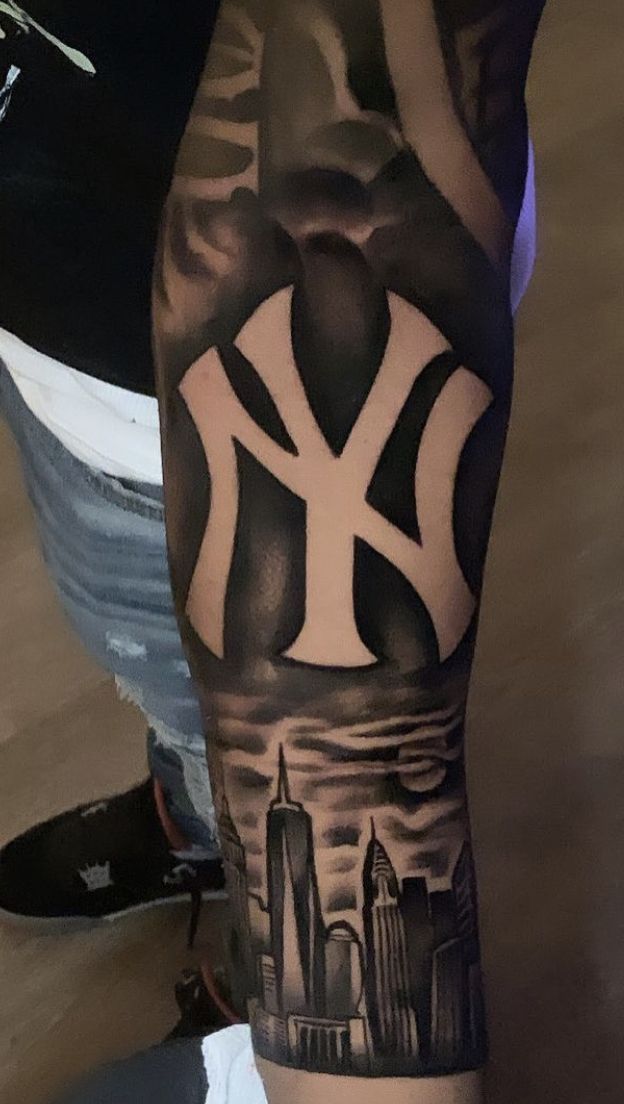 a man's arm with a new york yankees tattoo on it and the city skyline in the background