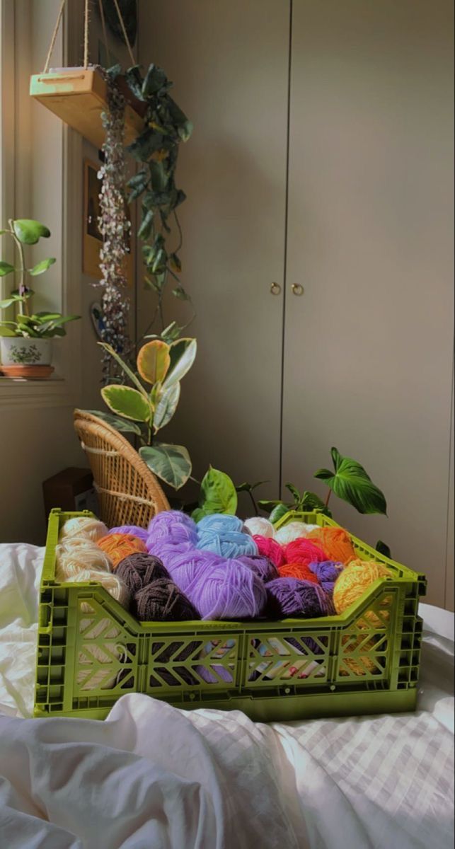 a basket filled with yarn sitting on top of a bed next to a mirror and potted plant