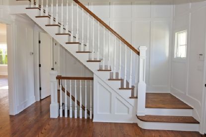 an empty room with stairs and hard wood flooring in the center, along with white painted walls