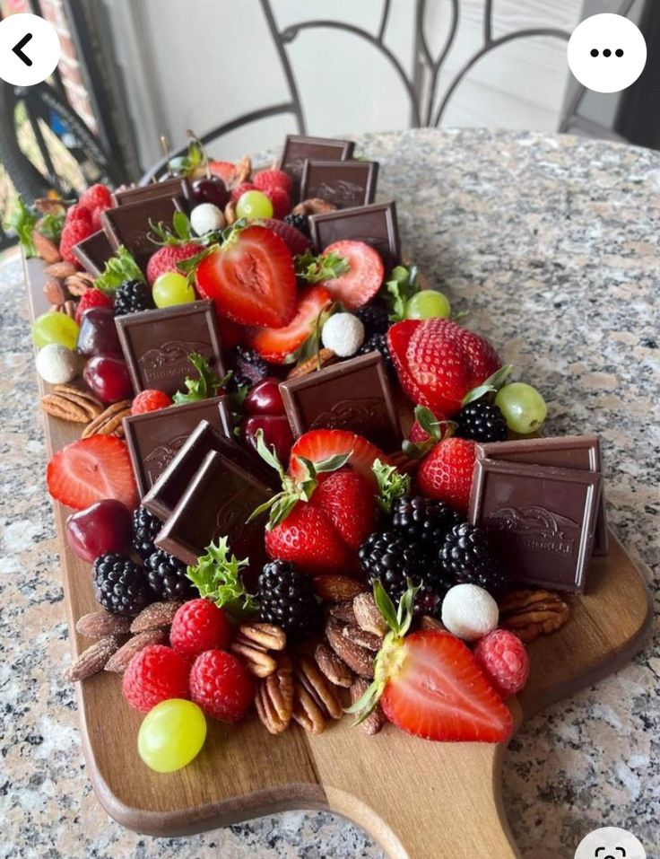 a wooden platter filled with chocolate covered strawberries and other fruit on top of a table