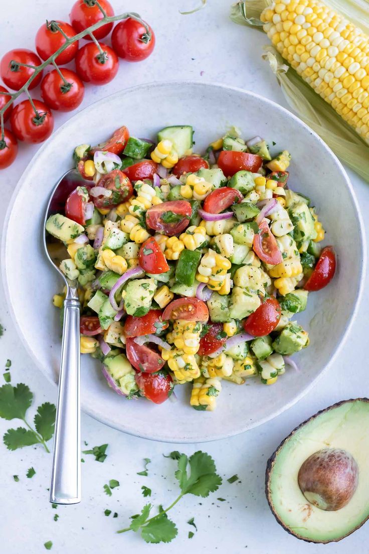 a salad with corn, tomatoes and avocado on a plate next to an avocado