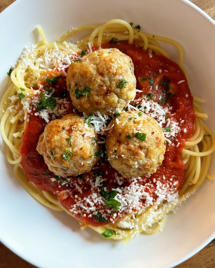 spaghetti with meatballs and parmesan cheese in a white bowl on a wooden table