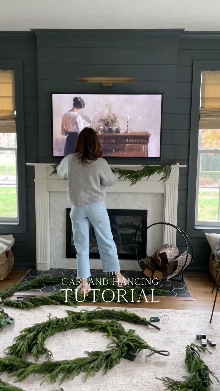 a woman standing in front of a fireplace with wreaths on the floor next to it