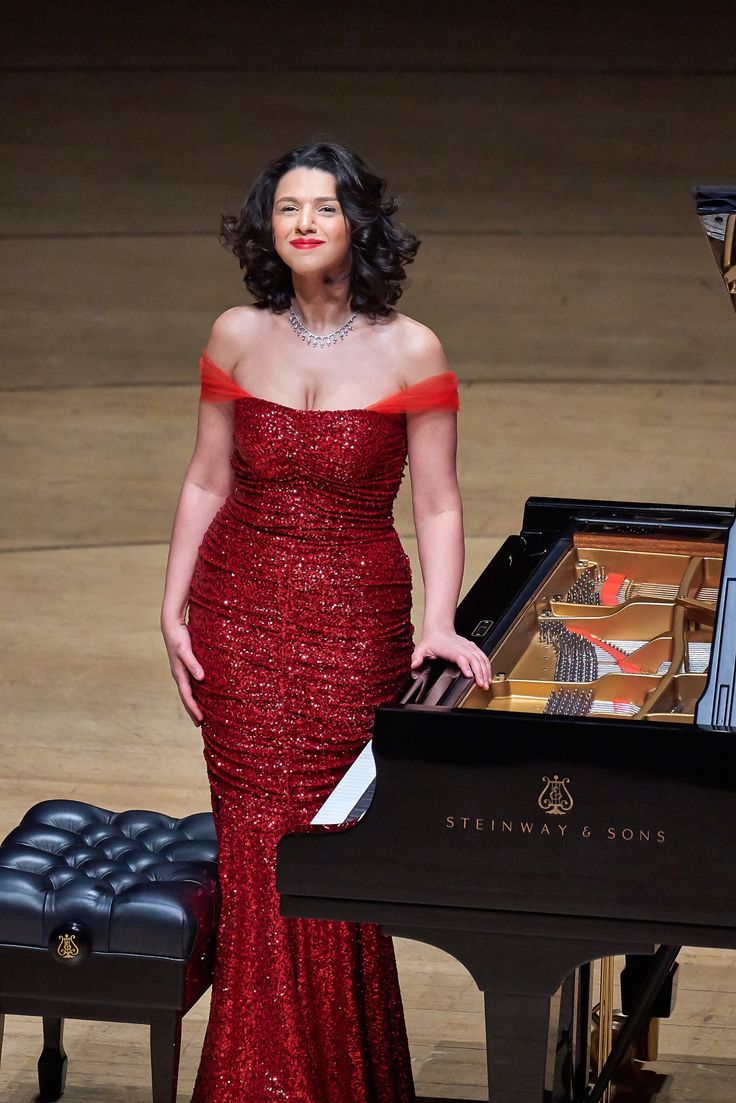 a woman in a red dress standing next to a piano