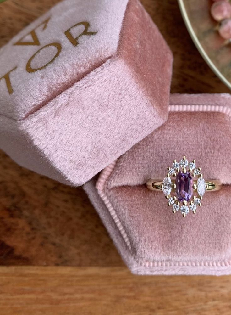 an engagement ring in a pink velvet box on top of a wooden table next to other jewelry items