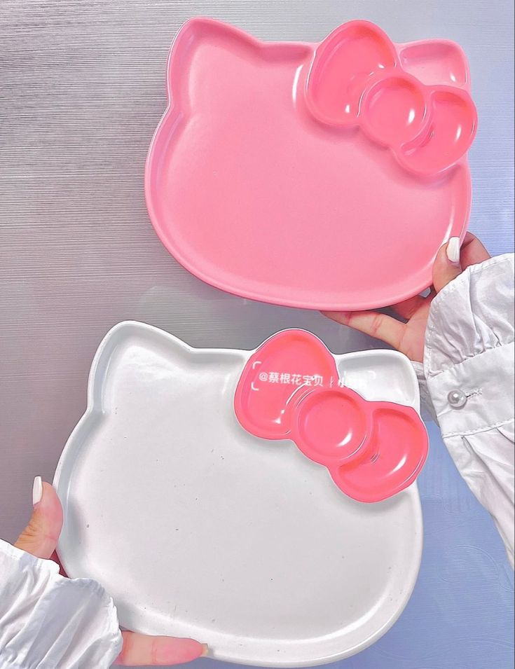 two hello kitty trays being held by someone's hand over a shiny surface