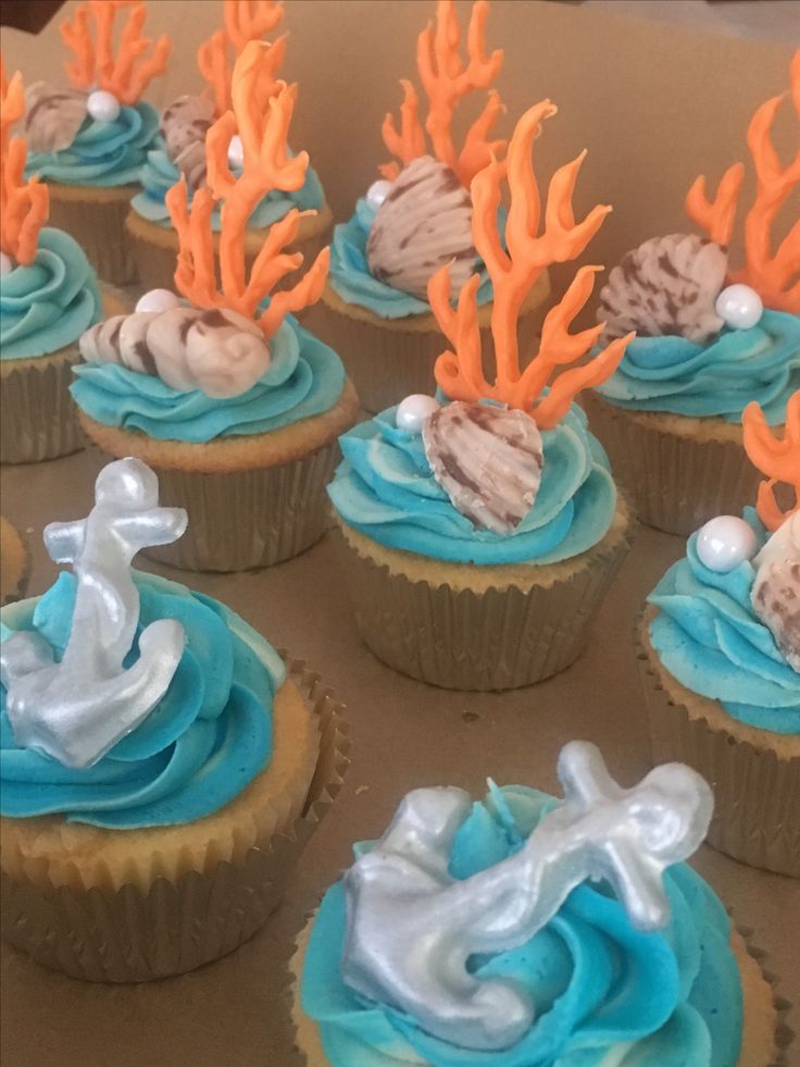 cupcakes decorated with blue frosting and orange corals are displayed in a box