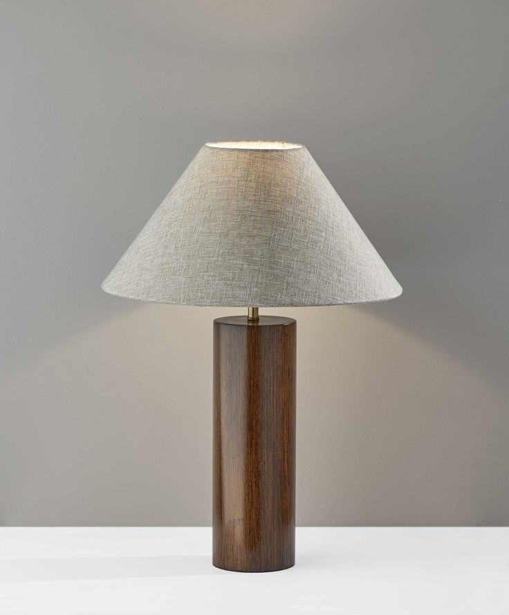 a wooden table lamp with a white shade on the top and grey wall behind it