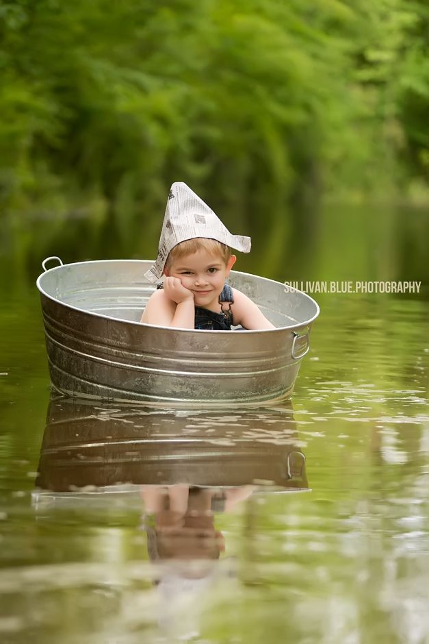 a little boy sitting in a metal boat on top of the water with trees in the background