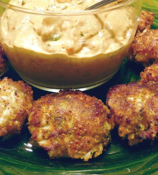 some crab cakes on a green plate with a bowl of dip in the middle,