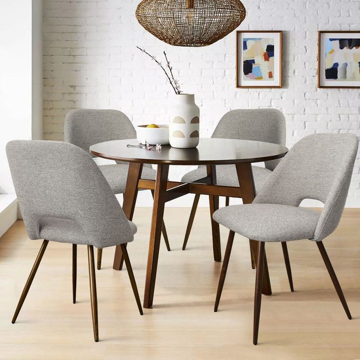 a dining table with four chairs and a vase on the top, in front of a white brick wall