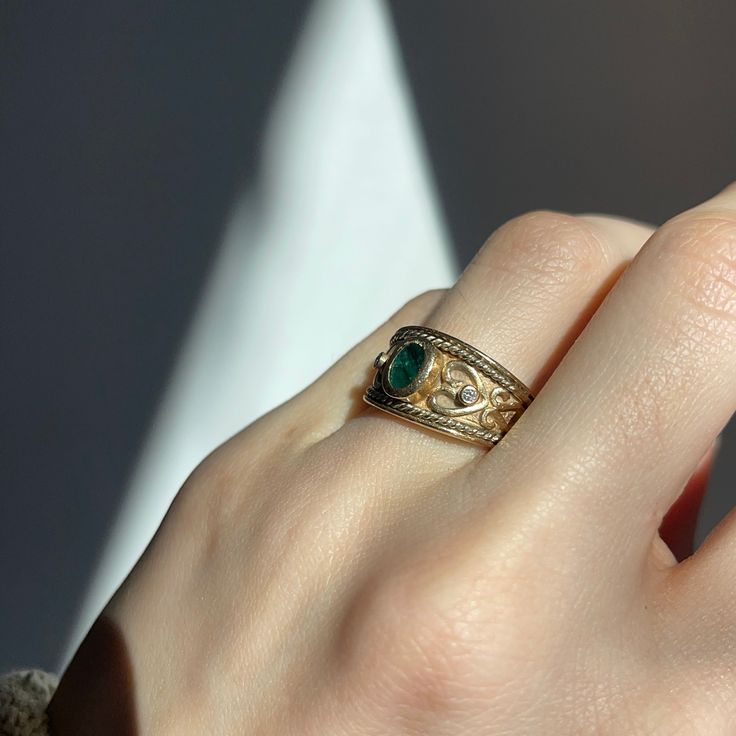 Estate/ vintage 14KT yellow gold Byzantine/ Etruscan design polished + textured matte-finish cigar band ring with genuine emerald + diamonds. Elegant, dark green emerald bezel-set front and center. Size 7 (1) Faceted oval-shaped, bezel-set emerald 5.5mm x 3.5mm emerald (2) Round Diamonds; .06 CT; SI clarity; H color Weighs 7.1 grams Solid Flat inside and may feel snugger on Measures: 10mm wide~ graduated back to 3mm Gold Emerald Signet Ring For Formal Occasions, Luxury Yellow Gold Signet Ring With May Birthstone, Luxury Yellow Gold Signet Ring For May Birthstone, Anniversary Green Signet Ring With Bezel Setting, Classic Gold Ring With Tsavorite, Yellow Gold Emerald Signet Ring With Bezel Setting, Elegant Green Signet Ring With Bezel Setting, Heirloom Emerald Ring For May Birthstone, Heirloom Emerald Signet Ring With Gemstone