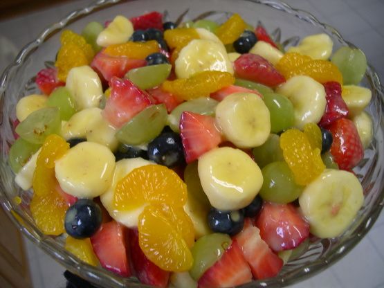 a fruit salad with bananas, oranges, grapes and strawberries in a glass bowl