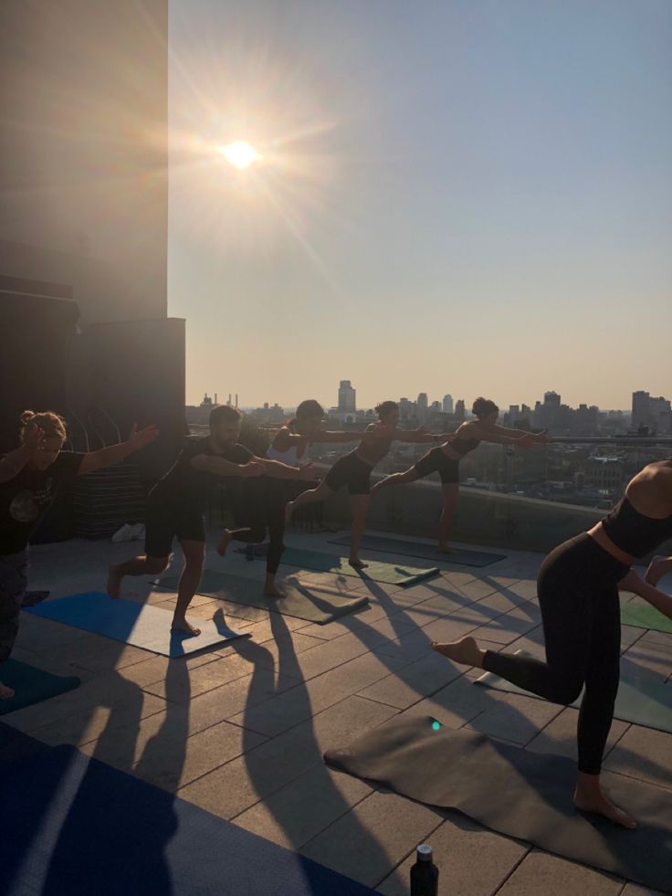 a group of people doing yoga on top of a roof in front of the sun