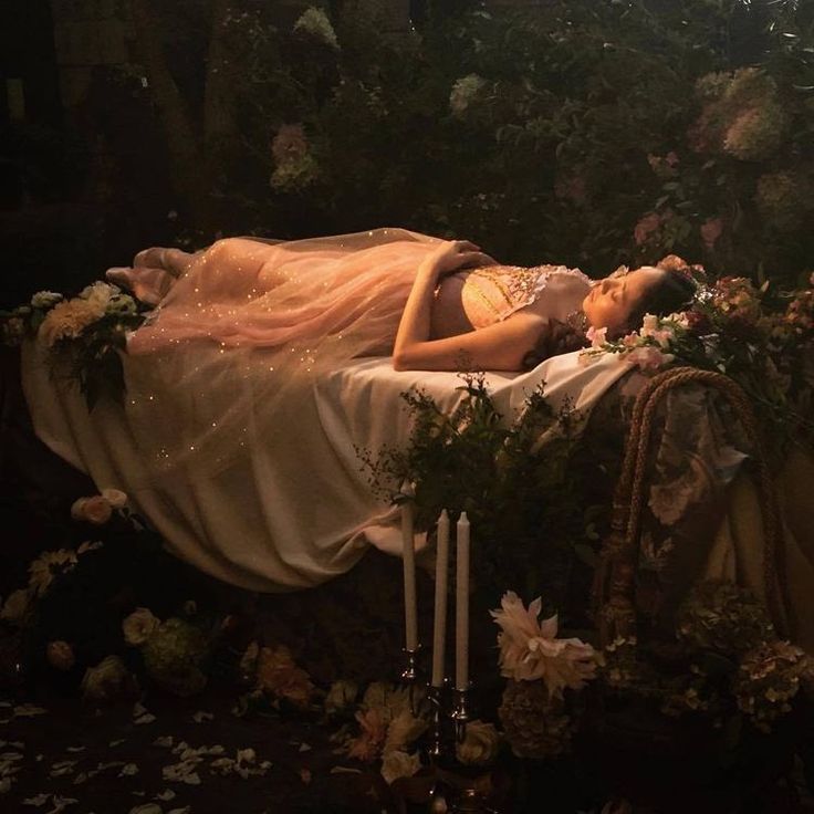 a woman laying on top of a bed covered in flowers and greenery next to candles