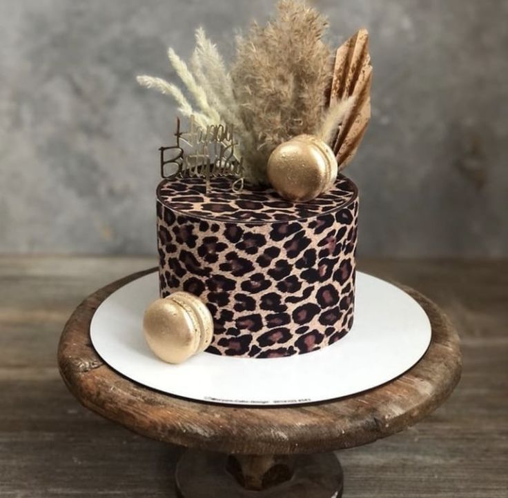 a leopard print cake on a wooden stand with feathers and gold decorations in the middle