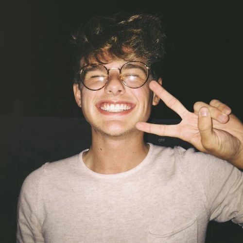 a young man making the peace sign with his fingers while wearing glasses and a t - shirt