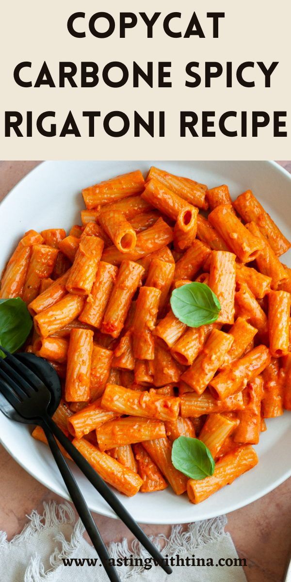 a white bowl filled with pasta and basil on top of a wooden table next to a black fork