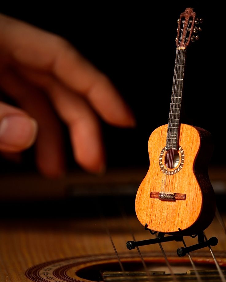 a small wooden guitar sitting on top of a table next to a person's hand