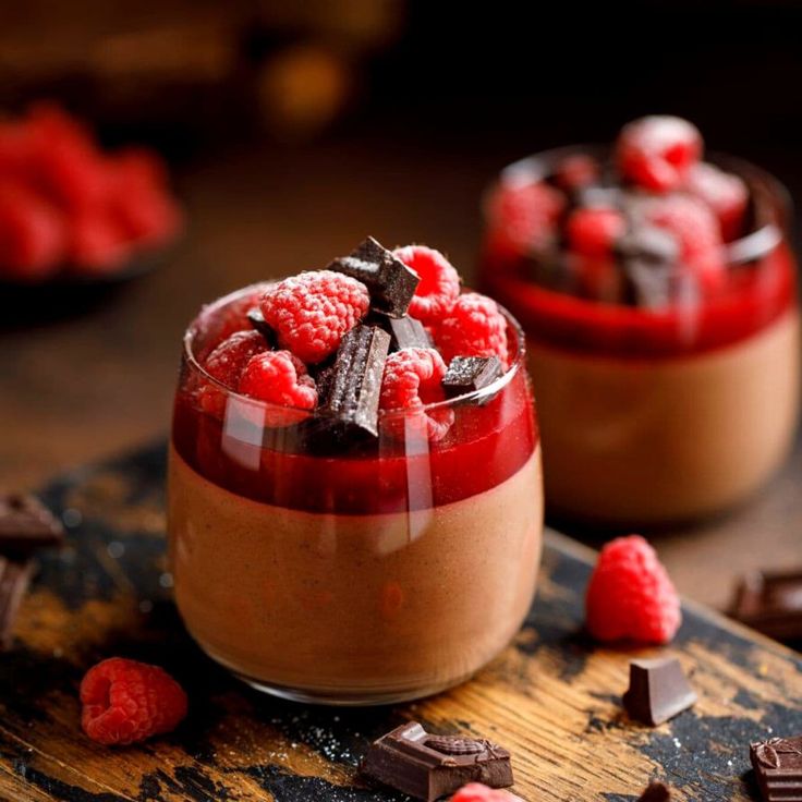 two desserts with chocolate and raspberries in them on a wooden table next to some candy