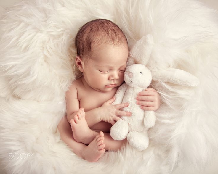 a baby sleeping with a stuffed animal in it's lap on a fluffy white blanket