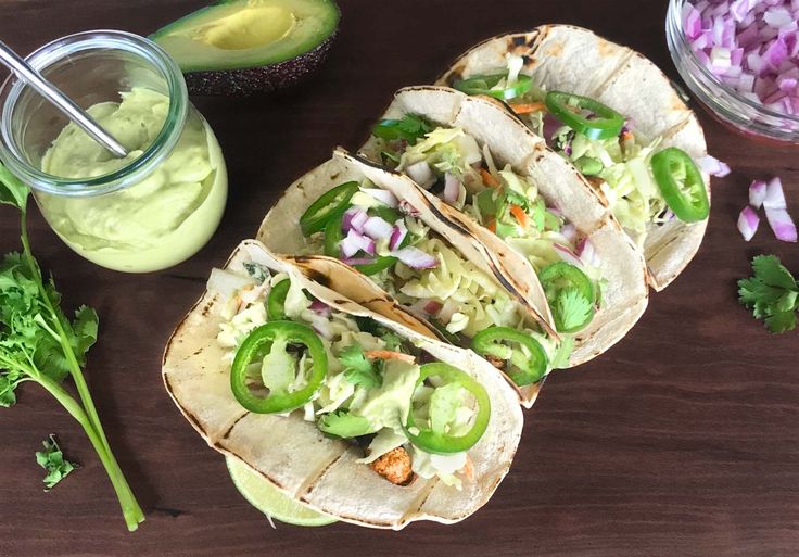 three tacos are sitting on a table next to an avocado and cilantro