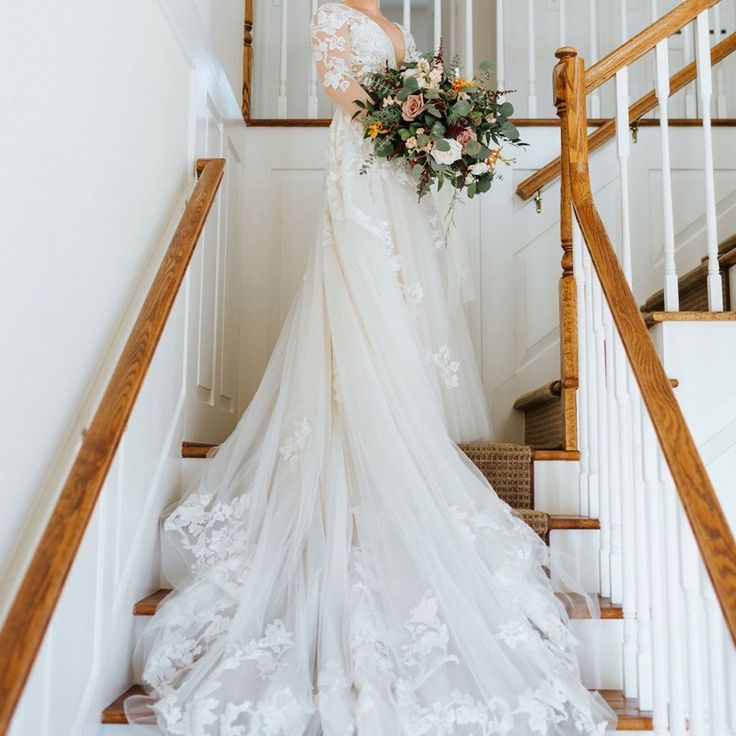 a woman in a wedding dress is standing on the stairs holding a bouquet and looking at the camera