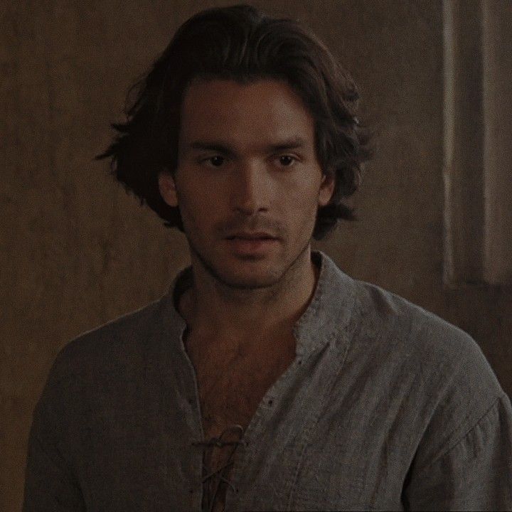 a man with long hair standing in front of a wall and looking at the camera