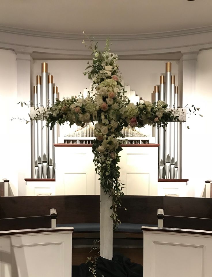 a cross decorated with flowers and greenery in front of an organ